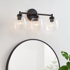 a bathroom vanity with three lights and a round mirror on the wall next to it