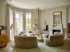 a living room filled with furniture and a fire place in front of two large windows