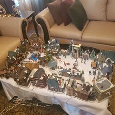 a table covered with lots of christmas village figurines on top of a white table cloth