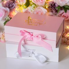 a pink and white box with a bow on it sitting in front of some flowers