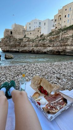 a person sitting at a table with food on it near the water's edge