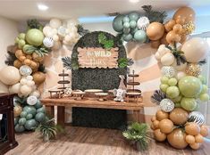 a table topped with lots of balloons next to a wall covered in greenery and jungle decorations