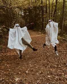 two people in white cloths are running through the woods with their arms outstretched and legs spread out