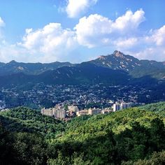 a view of a city in the distance with mountains in the foreground and clouds in the sky