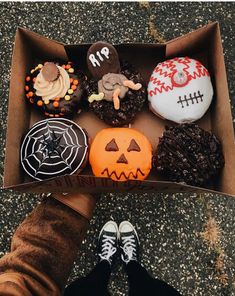 a box filled with lots of decorated donuts on top of a floor next to someone's feet