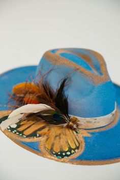 Be a sight for sore eyes with this royal blue rancher hat! Embellished with stunning gold accents and a golden Butterfly and feather combo, throw on this hat and give your look a kiss of style! This hat is ONE OF A KIND, created by our owner Stephanie. To receive item quicker, expedited shipping is available at checkout. Luxury Bohemian Hats With Feathers, Butterfly Burned Hat, Bohemian Gold Hat For Kentucky Derby, Gold Bohemian Hat For Kentucky Derby, Blue Fedora For Kentucky Derby And Country Events, Blue Hat For Kentucky Derby Festival, Blue Hat For Kentucky Derby, Custom Blue Hat For Kentucky Derby, Boho 2024