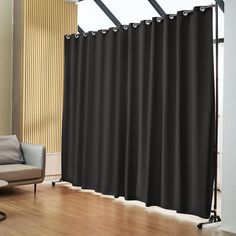 a living room with a couch, chair and window covered in black curtain panels next to a wooden floor