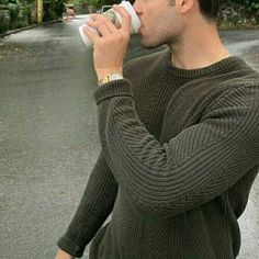 a man drinking from a cup while standing on the side of a road with trees in the background