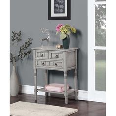 a small grey table with drawers and flowers on top in front of a gray wall