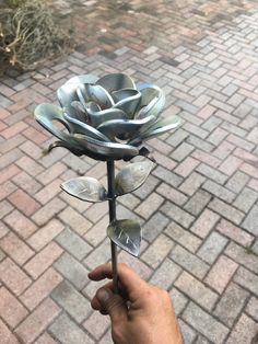 a hand holding a metal flower on top of a brick walkway