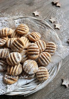 a glass bowl filled with cookies on top of a wooden table covered in powdered sugar