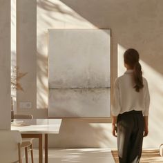 a woman standing in front of a large painting on the wall next to a table