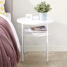 a white table with a potted plant on it next to a bed and pillows