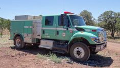 a green fire truck parked on the side of a dirt road