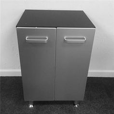 a black and white photo of a metal cabinet with wheels on the bottom, next to a wall