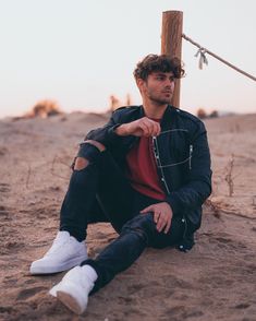 a man sitting in the sand with his hand on his hip and looking at the camera