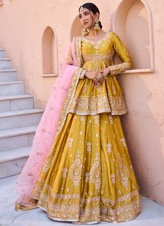 a woman in a yellow and pink lehenga standing next to a wall with her hands on her hips