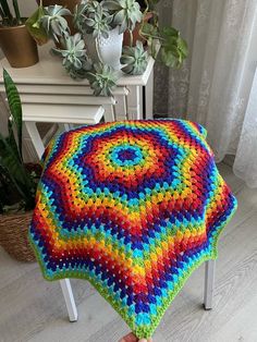 a multicolored crocheted blanket sitting on top of a stool next to a potted plant