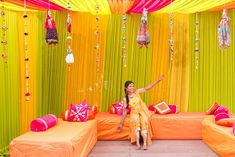 a woman sitting on an orange couch in front of a yellow and pink stage backdrop