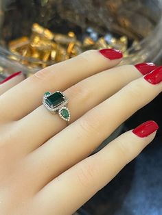 a woman's hand with red nail polish holding a green and white stone ring