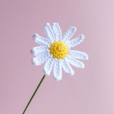 a crocheted white flower with yellow center on a pink background in the shape of a daisy