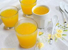 three glasses filled with orange juice sitting on top of a white table cloth next to utensils