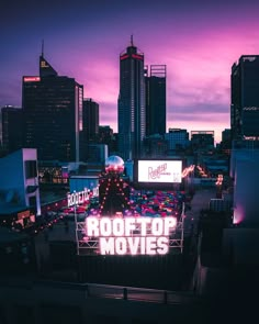 the roof top movies sign is lit up at night in front of city skylines