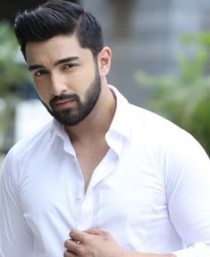 a man with a beard and white shirt is posing for the camera while holding his hand on his chest