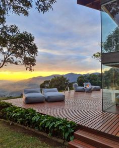 an outdoor deck with lounge chairs overlooking the mountains and trees at sunset or sunrise, in front of a modern home