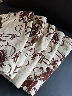 four napkins with brown and white designs are on a blue tablecloth next to a bottle