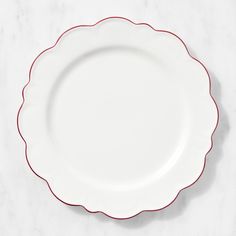 an empty white plate with red trim on a marble counter top, ready to be used as a place setting