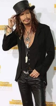 a man with long hair wearing a top hat and black leather pants at an event