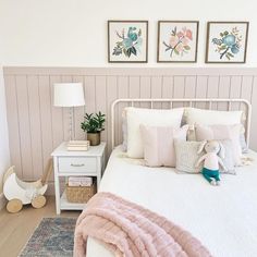 a white bed topped with pillows next to two framed pictures on the wall above it