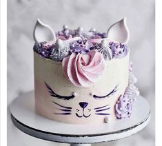 a white cake with pink frosting and purple icing on top, topped with a cat's face