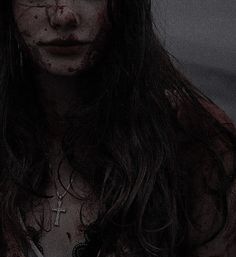 a woman with blood all over her face and cross on her chest is staring at the camera