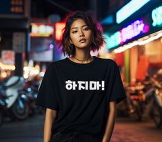 a woman standing in the middle of a street at night wearing a black t - shirt with korean writing on it