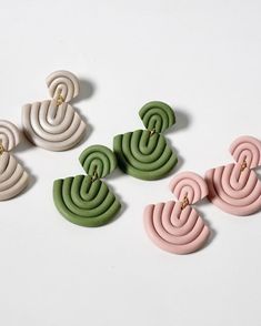 four pairs of earrings on a white surface with green and pink shapes in the middle