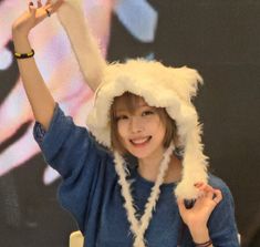 a young woman wearing a furry hat and holding her hands up in the air while smiling