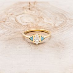 a yellow gold ring with blue and white stones in the center on a wooden surface