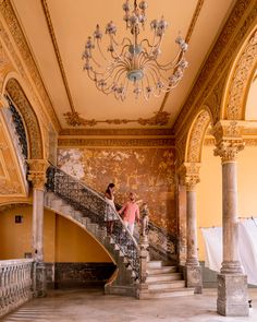 two people are standing on the stairs in an old building with chandelier and painted walls