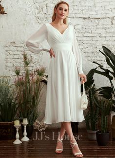 a woman wearing a white dress standing in front of some plants and potted plants