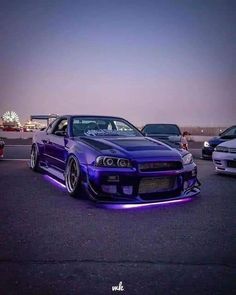 a purple car parked in a parking lot with other cars behind it at night time