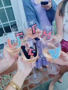 several people holding up wine glasses with the letters utf and m on them in front of a house