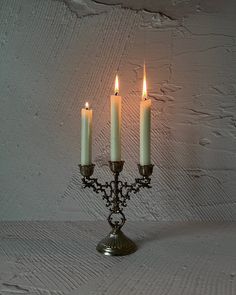 three candles are lit on a small metal candelabra against a white wall