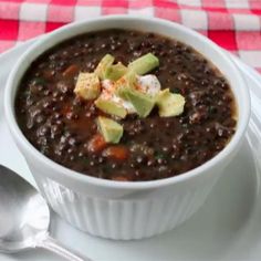 a white bowl filled with black beans on top of a plate next to a spoon