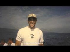 a man standing in front of the ocean wearing a hat