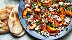 a blue plate topped with sliced peaches and feta cheese next to pita bread