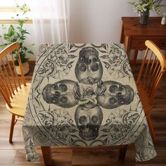 the table cloth has three skulls on it and is in front of two wooden chairs