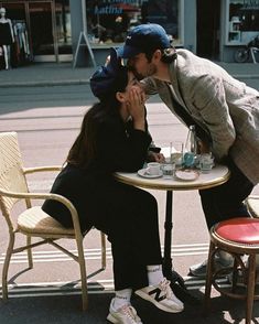 a man and woman sitting at a table with cups in front of each other on the street