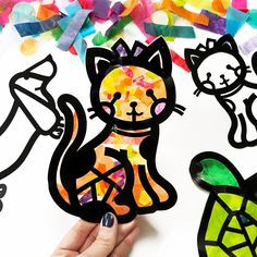 someone is holding up some paper cutouts with cats and turtle on them in front of confetti